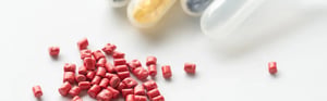 Rotes Kunststoffgranulat für Medical-Grade-Materialien vor Reagenzgläsern mit Proben auf weißem Untergrund