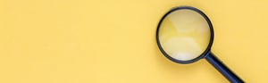 Schwarze Lupe auf gelbem Hintergrund als Symbol für Trenderkennung und Datenanalyse in der Post-Market Surveillance (PMS).