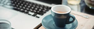 Eine Tasse Espresso auf einer Untertasse neben einem geöffneten Laptop auf einem Schreibtisch