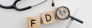 Holzbausteine mit der Aufschrift FDA neben einem Stethoskop zur Veranschaulichung der Anpassung von 21 CFR Part 820 (QMSR).