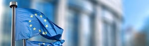 EU-Flaggen vor einem europäischen Regierungsgebäude als Symbol für Post-Market Surveillance (PMS), neue EU-Leitlinien, MDR-/IVDR-Compliance und regulatorische Anforderungen für Medizinprodukte.