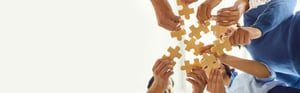 Team members collaborating by assembling puzzle pieces, symbolizing cross-functional teamwork, strategic partnership, and successful project integration in a professional business environment.