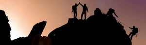 Bergsteiger unterstützen sich gegenseitig beim Erreichen eines Gipfels – Symbol für erfolgreiches Change Management und Teamarbeit im Qualitätsmanagement der Medizintechnik.